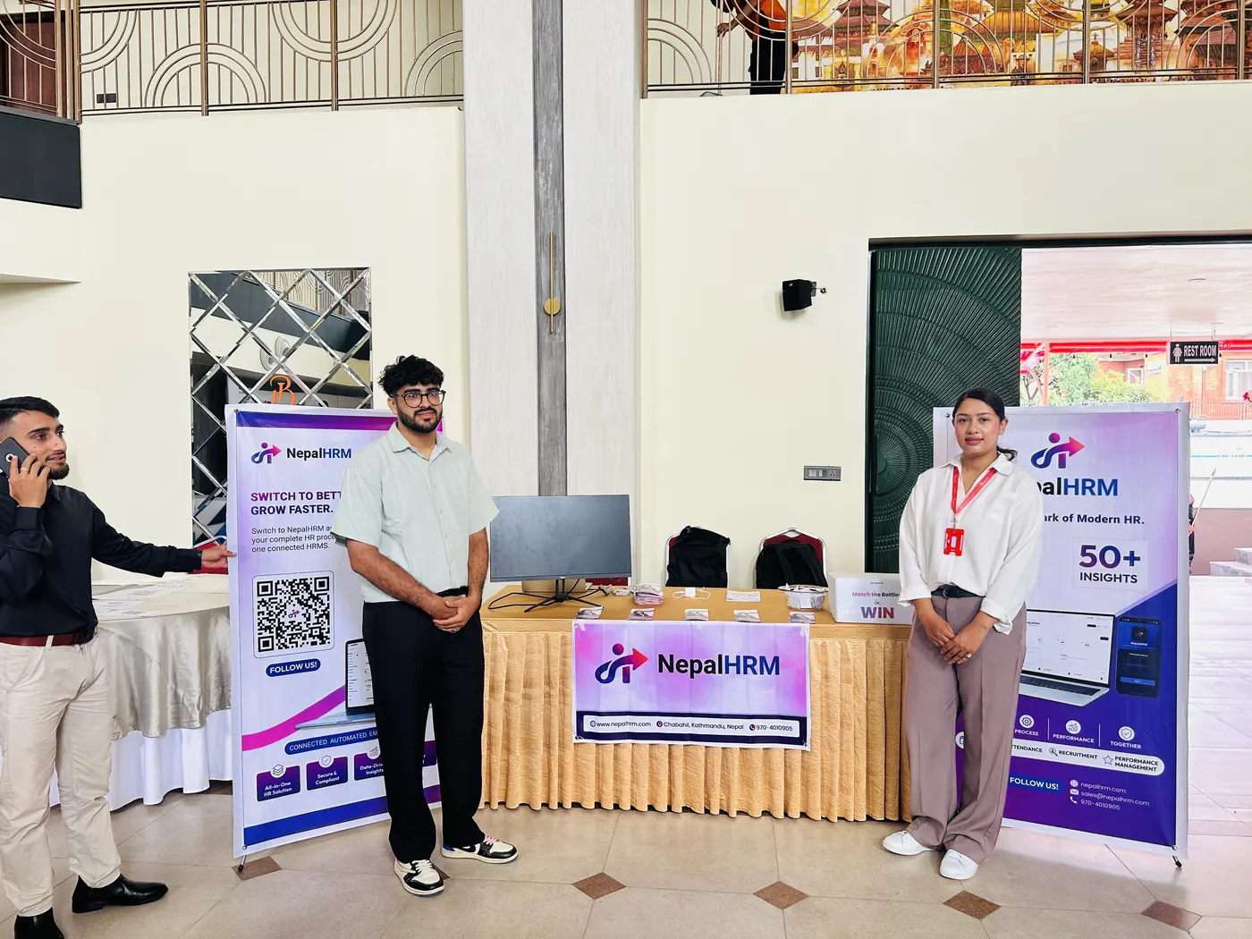 Two NepalHRM team members setting up the stall at Baneshwor Hills, with a NepalHRM standee, a table banner and a monitor in place.