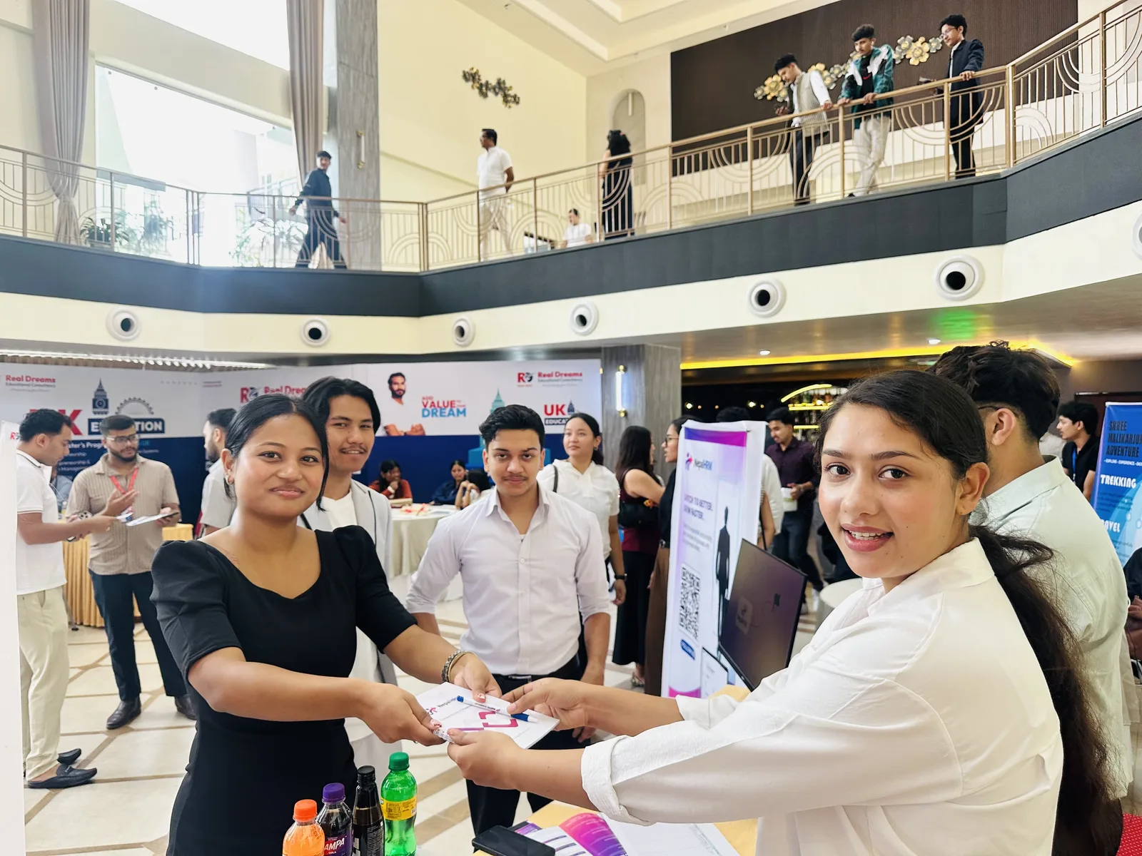 A NepalHRM team member handing a game prize to a visitor across the stall table, with the busy Idea Summit exhibition floor behind them.