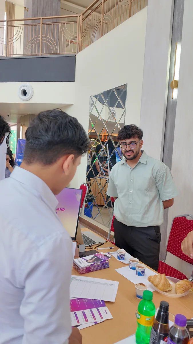A visitor talking to a NepalHRM team member across the stall, with the product running on a laptop and brochures fanned out on the table.