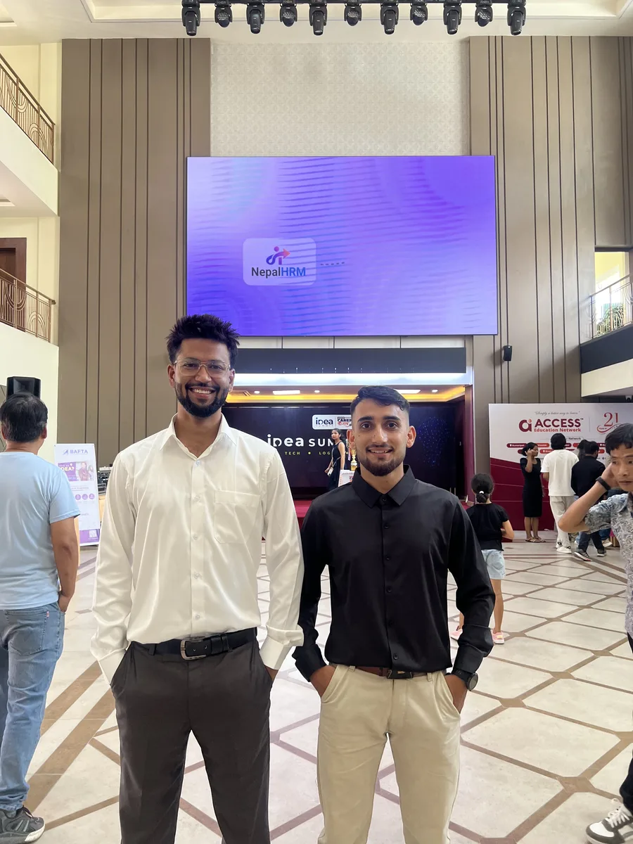 Two NepalHRM team members in front of the main event screen at Idea Summit 2026, which is displaying the NepalHRM logo.