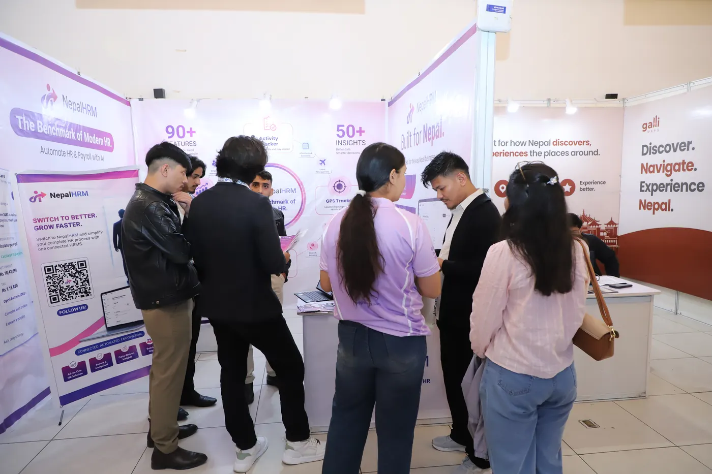 Visitors talking to the NepalHRM team at the NepalHRM stall at Nepal Fintech Expo 2026, with the lilac product panels behind them