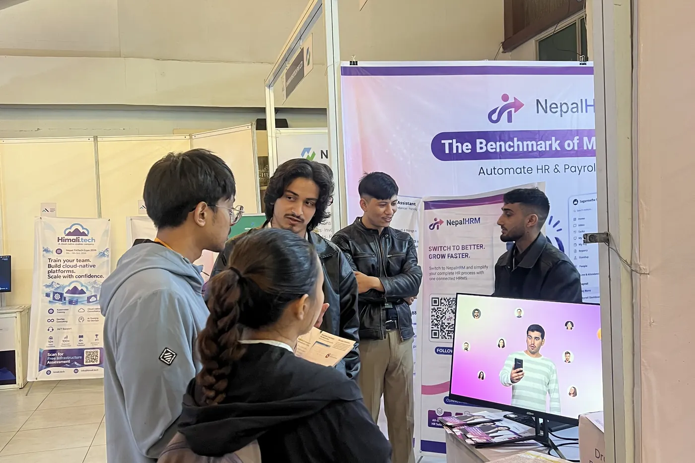 A group of young visitors gathered at the NepalHRM stall, looking at the product on a monitor while a team member talks them through it