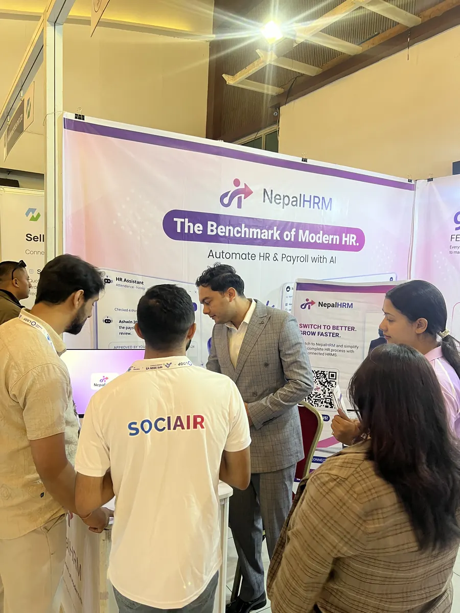 A NepalHRM team member in a grey suit talking a group of visitors through the product at the stall