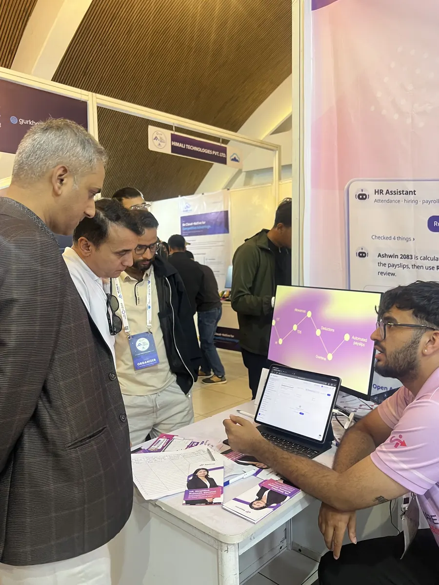 A NepalHRM team member showing the product on a laptop to visitors standing at the stall table