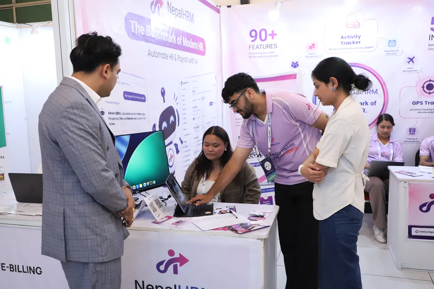 A NepalHRM team member demonstrating the product on a monitor to a visitor in a grey suit at the NepalHRM stall
